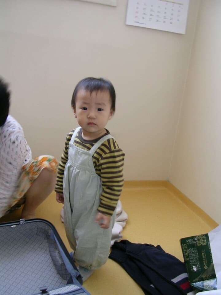 멜빵바지를 입고 거실에 서 있는 같은 시기의 모습